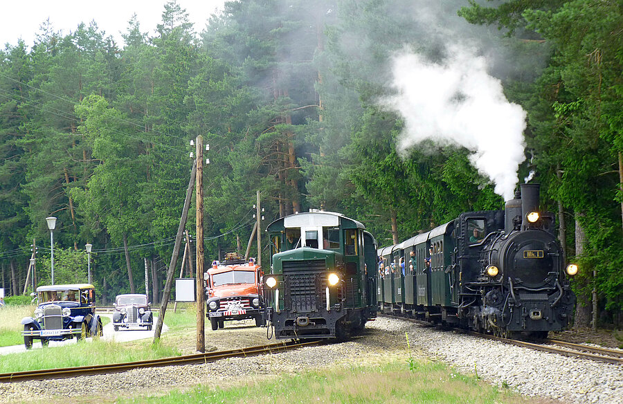 Dampfzug mit Oldtimern auf Straße und Schiene