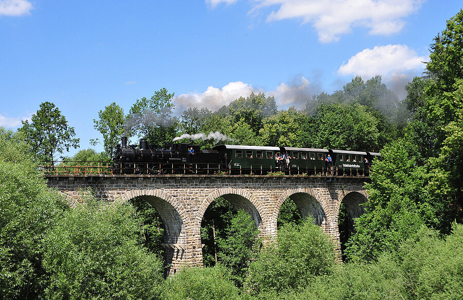 Rauchender Dampfzug fährt über ein Viadukt.