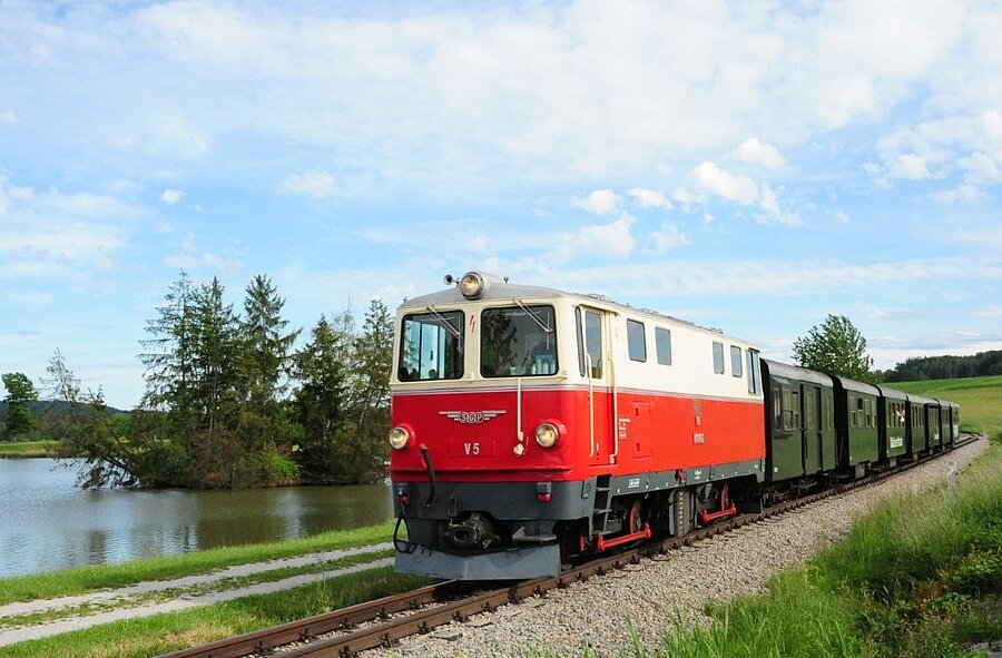 Rot weiße Diesellok fährt entlang eines Sees.