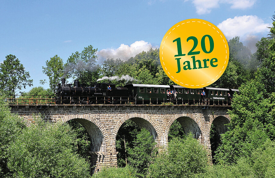 Rauchender Dampfzug fährt über ein Viadukt.