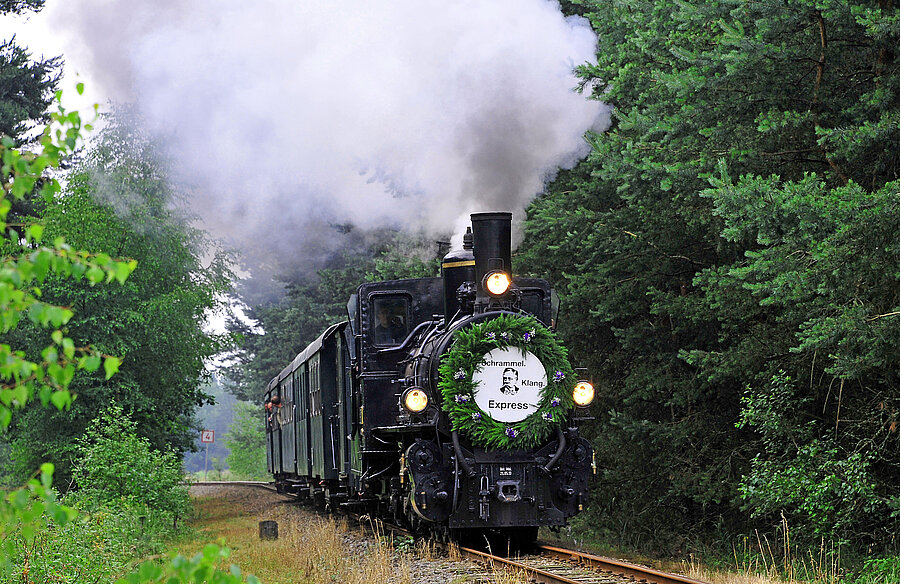 [Translate to English:] Dampfende Lok fährt durch Wald