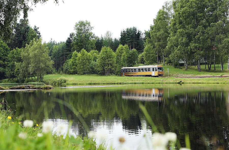 Der Diesel Triebwagen fährt entlang einer Seenlandschaft.