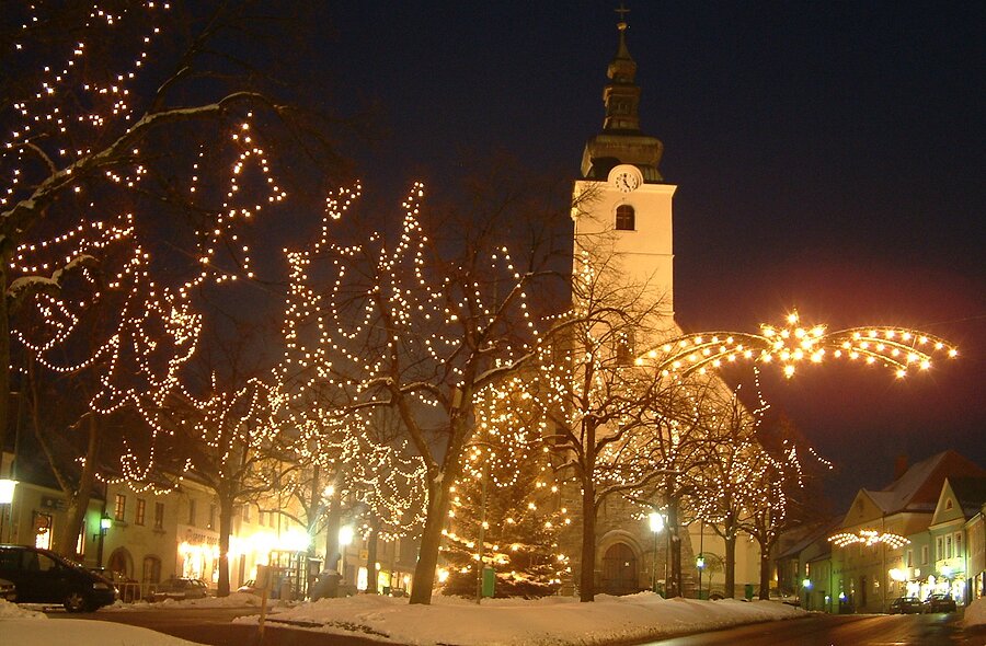 Weihnachtlich beleuchteter Marktplatz mit Kirche und geschmückten Bäumen bei Nacht in Litschau