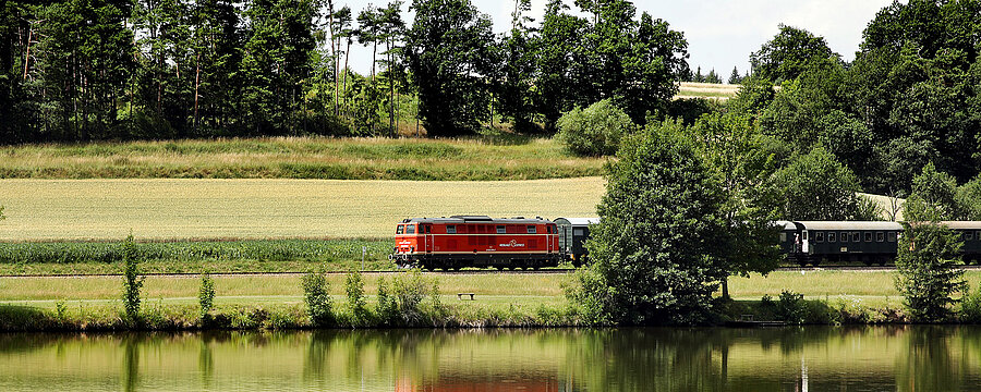 Roter Zug fährt durch Landschaft mit Teich