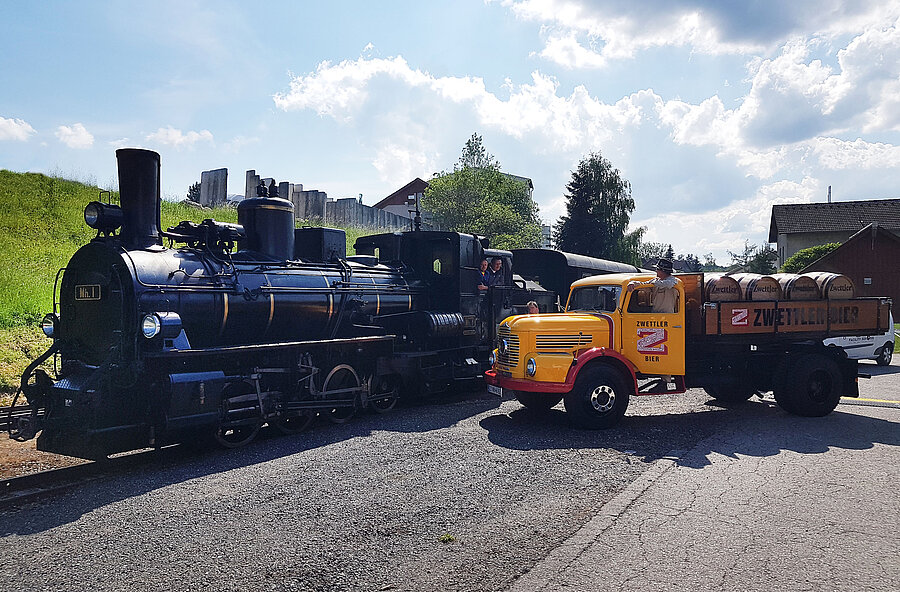 Die Dampflok steht neben einem Oldtimer Traktorimer