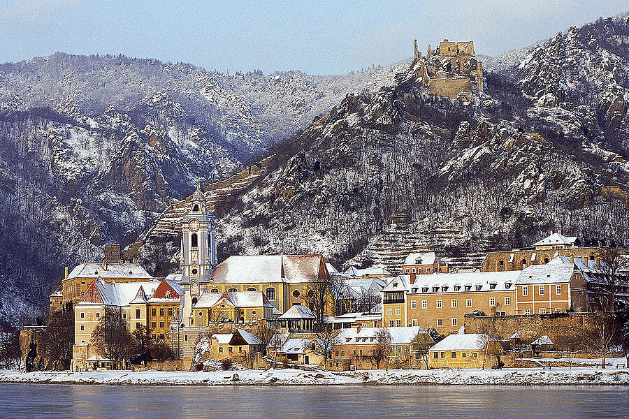 Verschneites Dorf am Flus mit hügeliger Landschaft