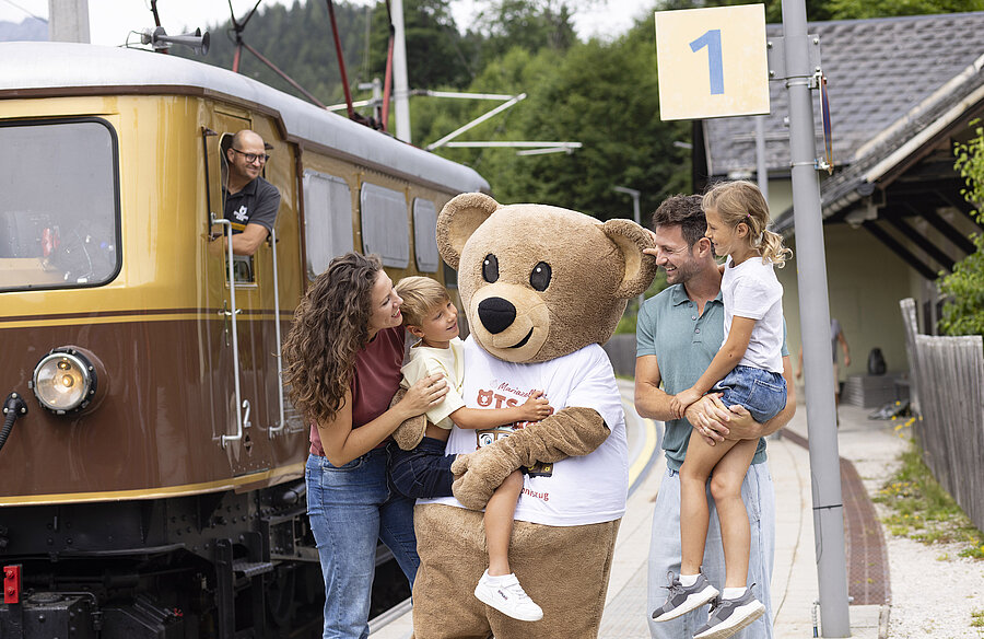 Auf dem Bahnsteig vor dem Zug steht eine Familie