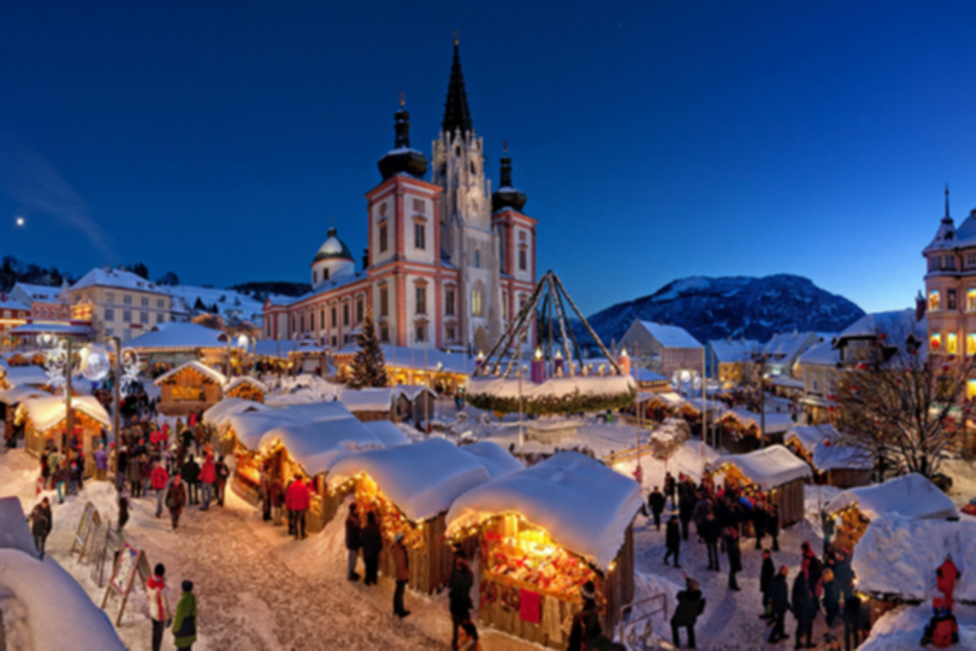 Verschneiter Adventmarkt vor der beleuchteten Basilika Mariazell in winterlicher Bergkulisse.